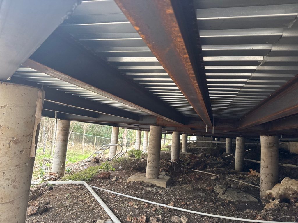 Concrete foundation piers providing structural support beneath a building, showcasing durability for Texas soil conditions, with visible steel beams and ground-level landscape.